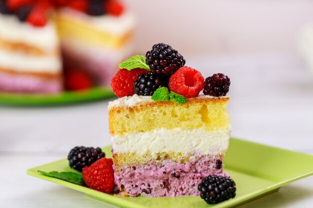 Pedaço de bolo de baga decorado com framboesas frescas e amoras-pretas em fundo branco.