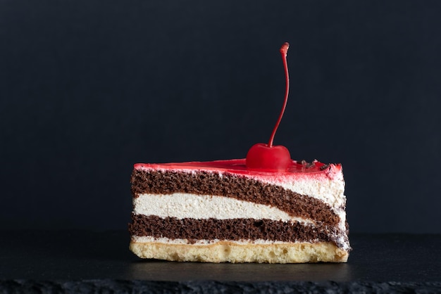 Pedaço de bolo de chocolate baunilha com cereja maraschino fundo preto vista lateral