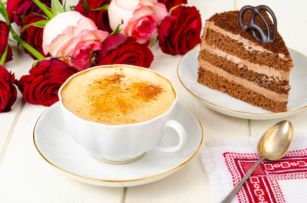 Pedaço de bolo de chocolate, cappuccino, flores na mesa.