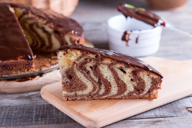 Pedaço de bolo de zebra com cobertura de chocolate na mesa de madeira