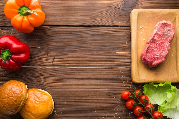 Foto pedaço de carne crua no tempero e legumes frescos na mesa de madeira, vista superior, ninguém. stek, pimenta e erva não cozida