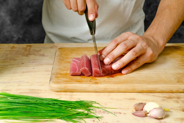 Foto pedaço de carne de atum na tábua de madeira e mão cortando com uma faca