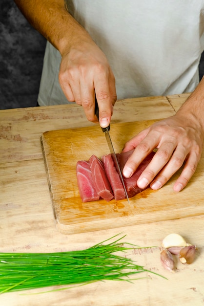 Foto pedaço de carne de atum na tábua de madeira e mão cortando com uma faca