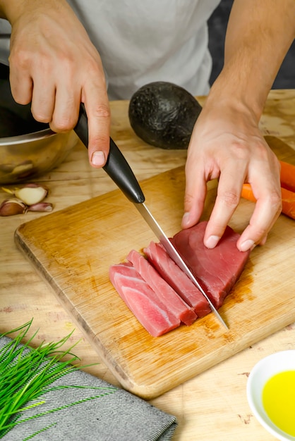 Foto pedaço de carne de atum na tábua de madeira e mão cortando com uma faca