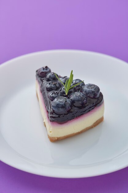 Pedaço de cheesecake de mirtilo na chapa branca sobre fundo violeta