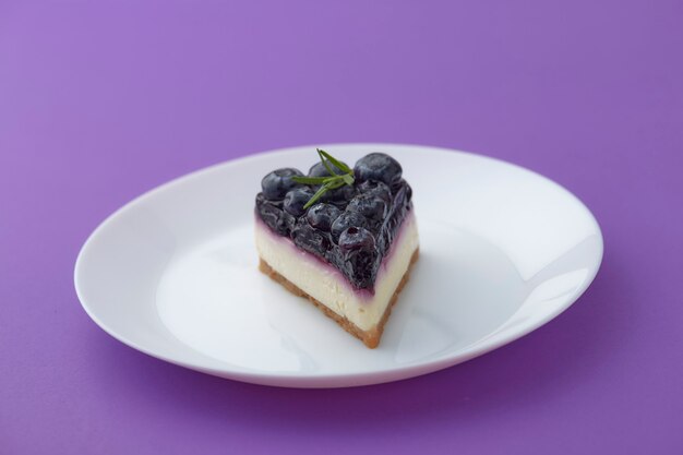 Pedaço de cheesecake de mirtilo na chapa branca sobre fundo violeta