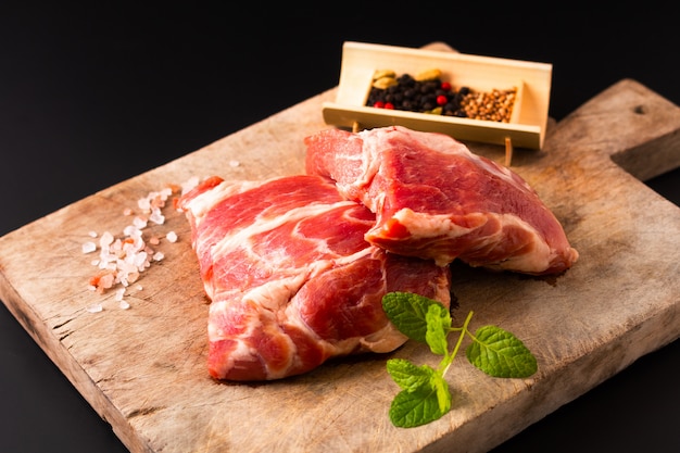 Pedaço de conceito de comida sem osso colarinho de porco na tábua com especiarias em fundo preto com espaço de cópia