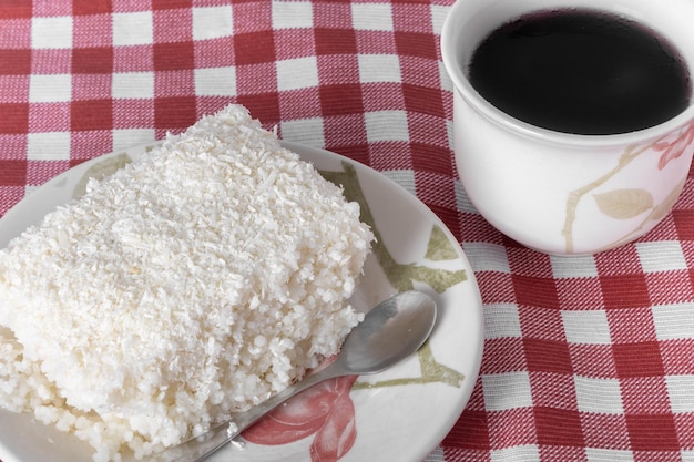 Pedaço de cuscuz em pires de porcelana sobre toalha xadrez Prato típico brasileiro feito com leite de tapioca, açúcar e leite de coco Com xícara de café