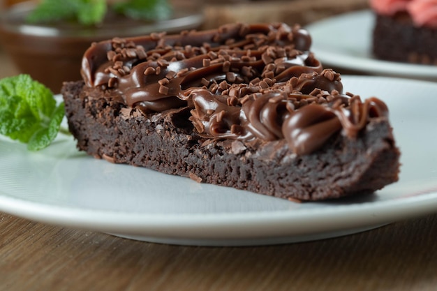 Pedaço de fatia de brownie de chocolate com morango e chocolate Mesa de madeira com menta e lascas de chocolate ao fundo