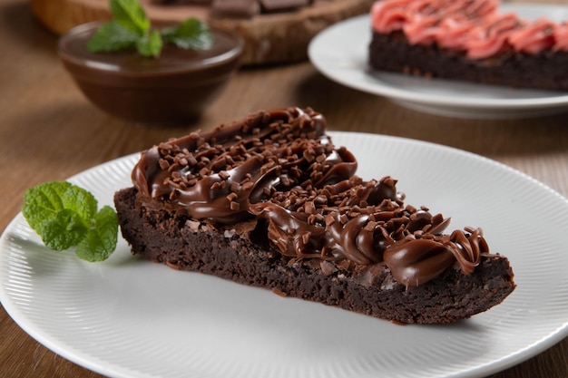 Pedaço de fatia de brownie de chocolate com morango e chocolate mesa de madeira com menta e lascas de chocolate ao fundo