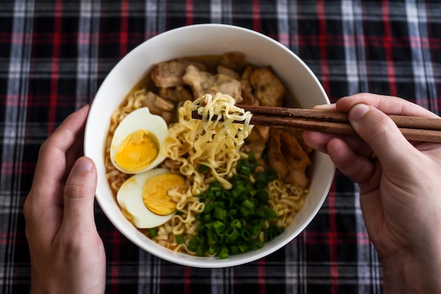 Pedaço de macarrão em pauzinhos com ramen japonês e mãos masculinas