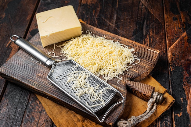 Pedaço de queijo semiduro e queijo ralado com ralador fundo de madeira vista superior