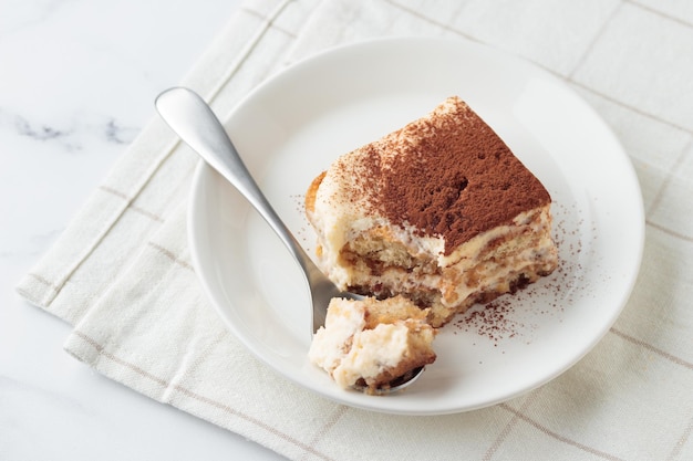 Pedaço de sobremesa de bolo tiramisu caseiro em um fundo de mármore branco