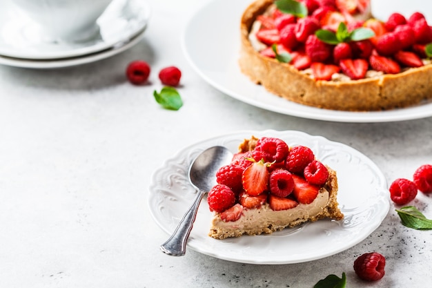 Pedaço de torta de berry com framboesas, morangos e creme na chapa branca