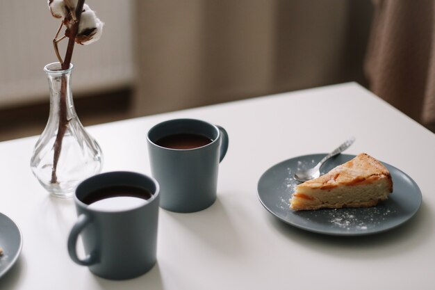 pedaço de torta de maçã no prato com uma xícara de café na mesa branca