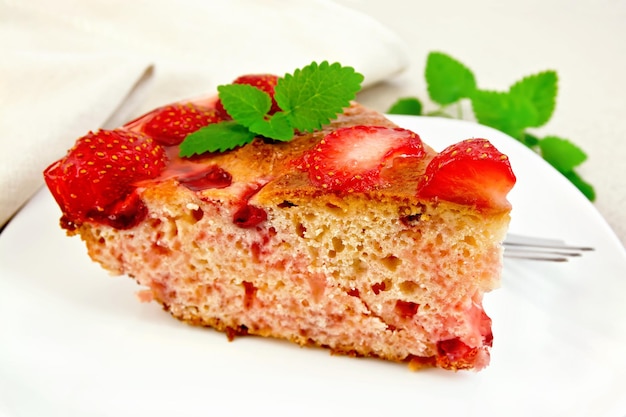 Pedaço de torta doce com morango, beijinho, geléia e hortelã, um garfo na chapa branca nas placas de madeira de luz de fundo