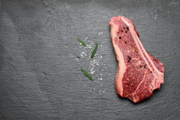 Pedaço fresco de carne bovina crua, bife striploin repousa sobre um quadro negro com especiarias, vista de cima