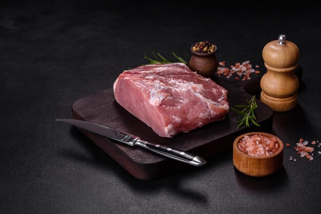 Pedaço fresco de carne de porco crua com sal de especiarias e ervas em uma tábua de madeira