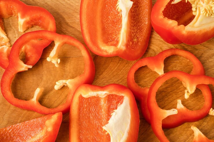 Foto pedaços cortados, pedaços de lóbulos de pimenta doce vermelha espalhados sobre uma tábua de madeira