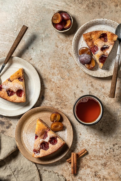 Pedaços da torta de bolo de ameixa do The New York Times polvilhada com açúcar de confeiteiro para chá em plano de fundo texturizado marrom vista superior do conceito de festa do chá de outono