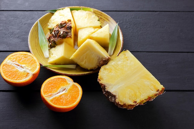 pedaços de abacaxi e metades de laranja em tábuas de madeira preta frutas de abacaqui e laranjas em fundo escuro