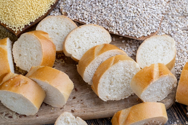 Pedaços de baguete de trigo em uma placa de corte Pedaços de baguete de trigo com cereais secos crus e cevada
