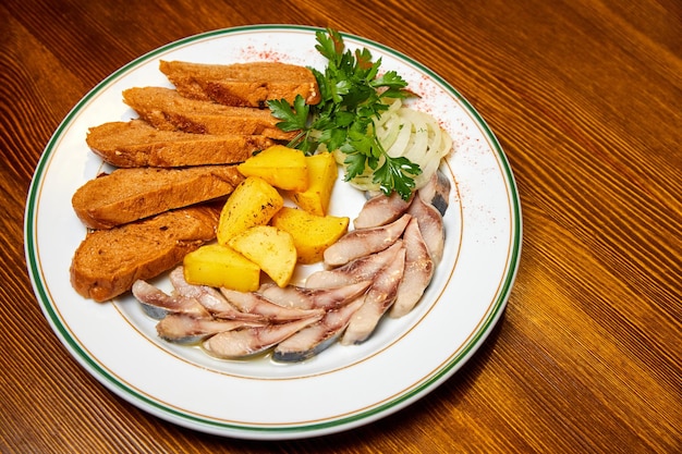 Pedaços de batatas de arenque em conserva pão cebolas e verduras em um prato branco