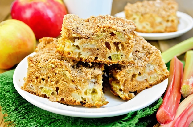 Pedaços de bolo doce com ruibarbo e maçãs em um guardanapo verde, copo no fundo de tábuas de madeira