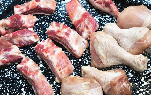 Pedaços de carne crua e pernas de frango em uma assadeira antes de cozinhar