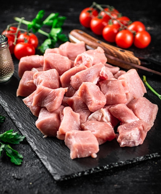 Pedaços de carne de porco crua em uma placa de pedra com salsa tomate e especiarias