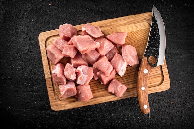 Pedaços de carne de porco crua em uma tábua de madeira com uma faca