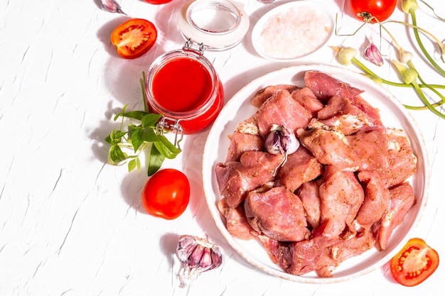 Pedaços de carne de porco crua, tomates, especiarias e ervas. Ingredientes para cozinhar alimentos saudáveis em um fundo de massa branca. Conceito de processo culinário, luz forte da moda, sombra escura, vista superior