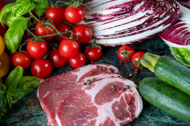 Pedaços de carne fresca, temperos e vegetais variados em um tabuleiro de mármore verde escuro