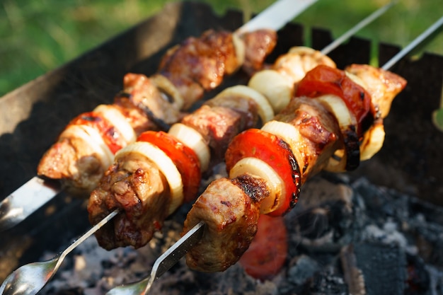 Pedaços de carne marinada com tomate e cebola em espetos de metal cozidos em uma churrasqueira no carvão