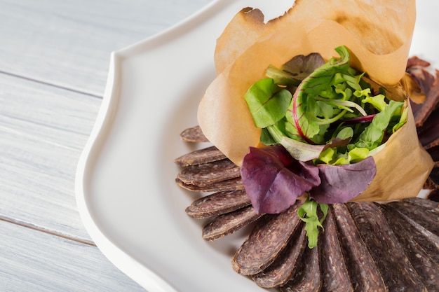 Pedaços de carne saborosa e salada no prato e mesa de madeira branca