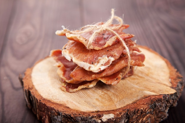 Pedaços de carne seca em uma pilha amarrada com barbante mentem sobre um corte de uma árvore em um fundo de madeira.