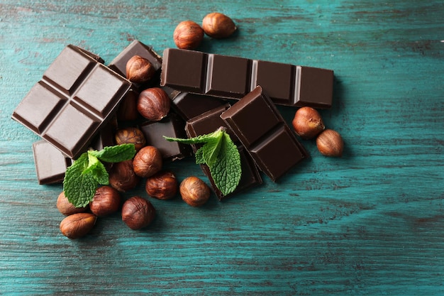Pedaços de chocolate com nozes na cor de fundo de madeira