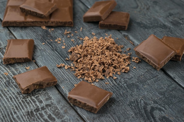 Pedaços de chocolate inteiro e chocolate ralado em uma mesa de madeira preta