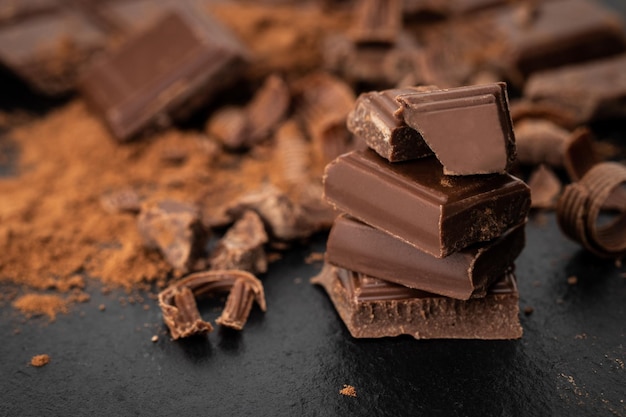 Pedaços de chocolate quebrados e cacau em pó em um fundo escuro.