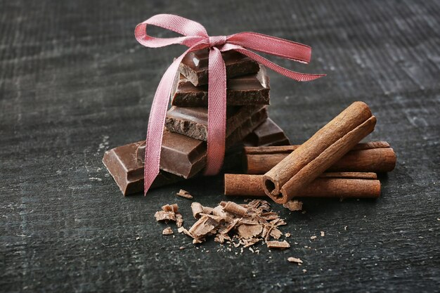 Pedaços de chocolate quebrados e paus de canela em fundo de madeira