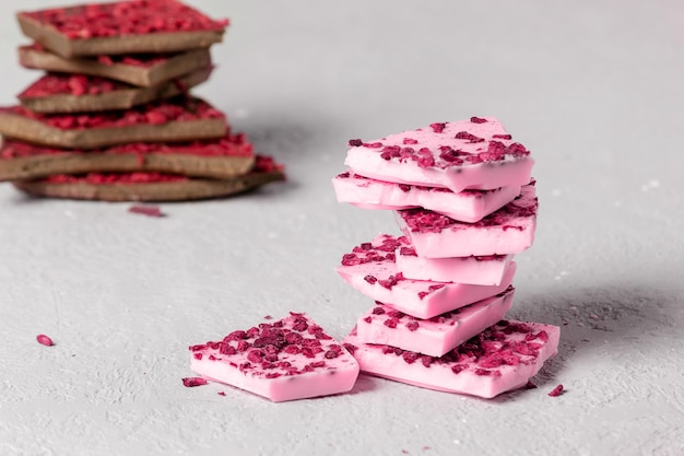 Pedaços de chocolate rosa e ao leite na moda com pedaços de frutas e frutas estão em cima de cada