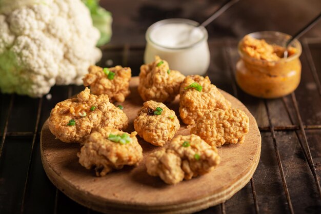 Pedaços de couve-flor frita com molhos veganos em um prato sobre um fundo escuro Comida de asas de couve-flor