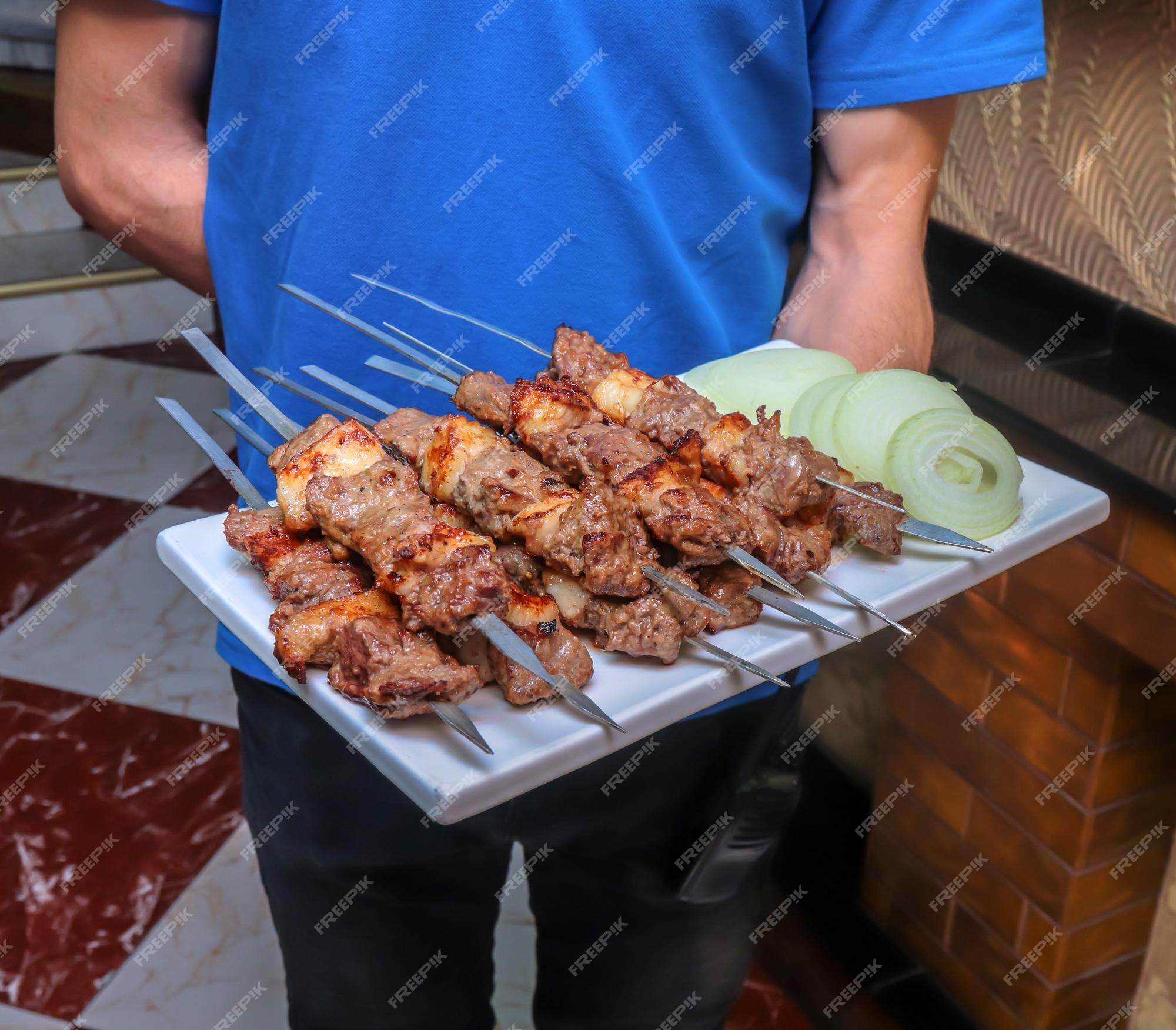 Pedaços de espetos de carne frita em um café em uma bandeja nas mãos de um  garçom