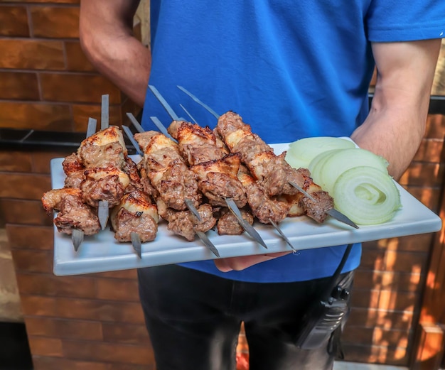 Pedaços de espetos de carne frita em um café em uma bandeja nas mãos de um  garçom