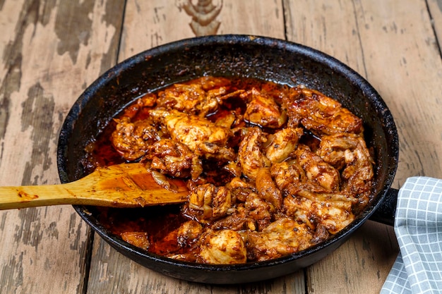 Pedaços de frango assado em molho em uma frigideira com uma espátula de madeira