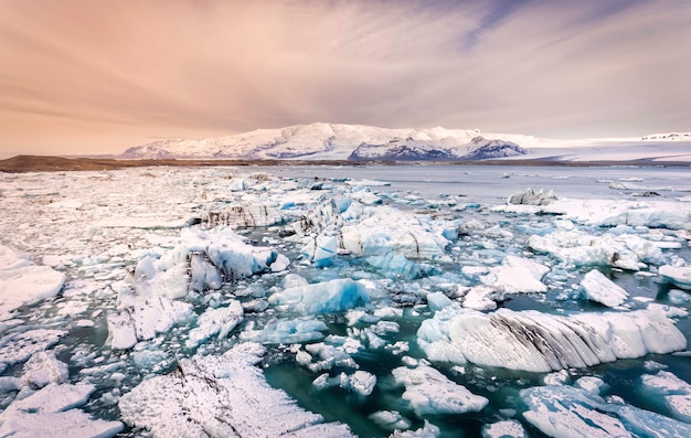 Pedaços de gelo espalhados por uma lagoa glaciar na Islândia com montanhas cobertas de neve