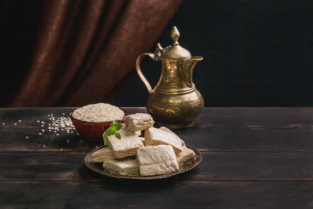 Pedaços de halva de tahine, sementes de gergelim em uma tigela, uma jarra vintage