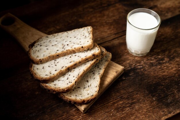 Pedaços de pão com sementes e um copo de leite Fundo de madeira escuro Café da manhã da manhã Comida saudável