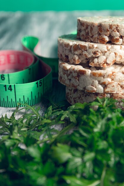 Pedaços de pão estaladiço perto de medir a fita e a rúcula verde no cinza.