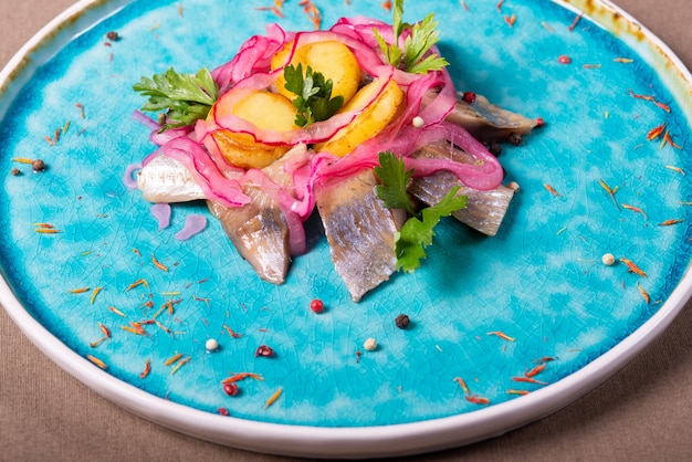 Pedaços de peixe arenque em um prato azul com batatas e salsa